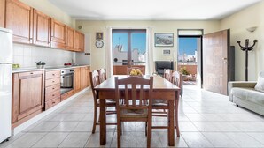 A spacious kitchen with wooden cabinets, a dining table with chairs, and a view through an open door to a balcony. - Appartamento Terrazza by BarbarHouse (Porto Cesareo)