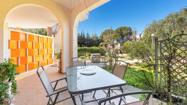An outdoor patio with a glass table and chairs, surrounded by a garden with various plants and a decorative wall. - I Sognatori - Bilo Plus by BarbarHouse (Torre Squillace)