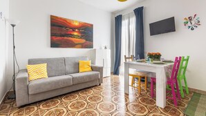 A living room with a sofa, a dining table, colorful chairs, a TV, and a painting on the wall. - I Sognatori - Bilo Plus by BarbarHouse (Torre Squillace)