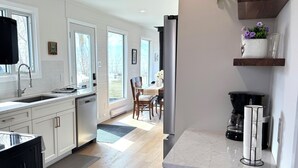 A modern kitchen with white cabinetry, a built-in dishwasher, and a dining area with a table and chairs. - BEACHFRONT COTTAGE *fully renovated* (Saint Laurent)
