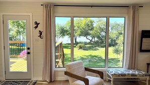 A room with a large window, a wooden chair, a bench, and a door with a view of a green outdoor area. - BEACHFRONT COTTAGE *fully renovated* (Saint Laurent)