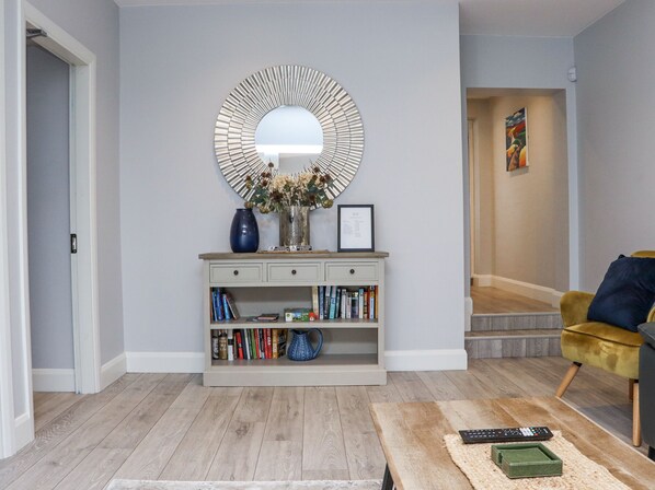 A living room with a wooden floor, a console table with books, a mirror, and a yellow armchair.