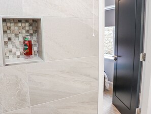 A bathroom with a tiled wall, a shelf with a bottle, and a door.