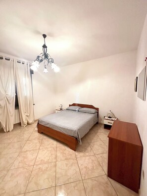 Quarto com cama, mesa de cabeceira, cómoda de madeira e luminária pendente.