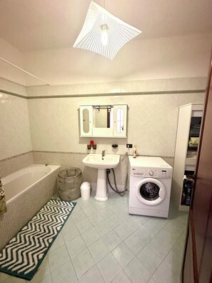 Uma casa de banho com banheira, pia e máquina de lavar roupa.