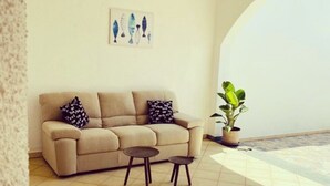 Una sala de estar con un sofá color beige, dos mesitas, un tapete decorativo y una planta en maceta.
