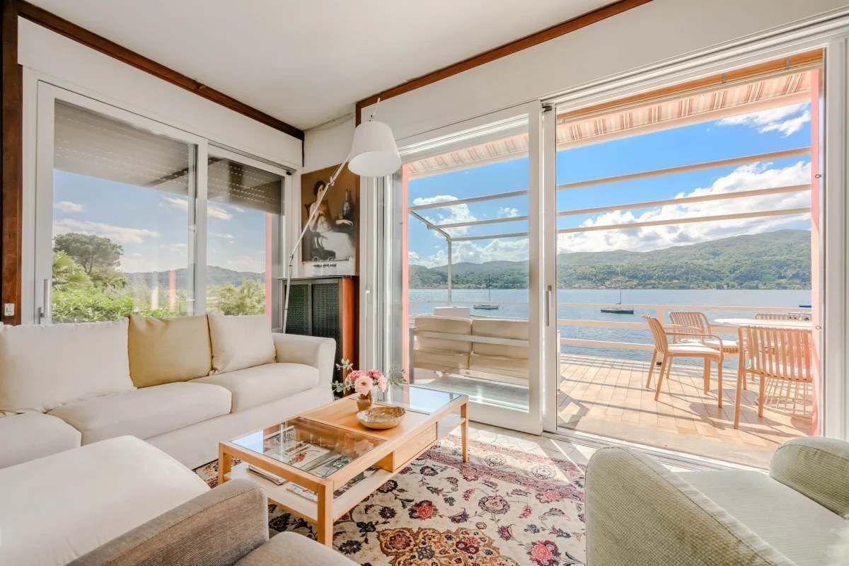 A spacious living area with a sofa, coffee table, and a view of a lake through large sliding glass doors.
