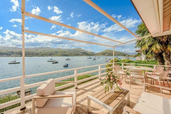 A terrace with outdoor seating and a view of a lake with boats. - Italian Lakes Lakeside Villa With Direct Lake Access (Ranco)
