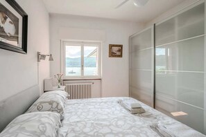Een slaapkamer met een bed, een raam, een radiator, een nachtkastje met een lamp en een lijst met een afbeelding aan de muur.