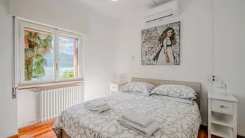 A bedroom with a bed, a nightstand, a window with a view, and an air conditioning unit.