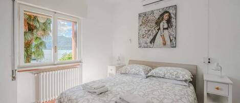 Un dormitorio con cama, mesita de noche, ventana y unidad de aire acondicionado.