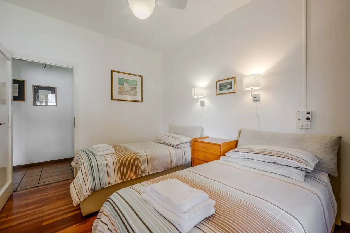 Habitación de hotel con dos camas, piso de madera, una puerta y cuadros en las paredes.