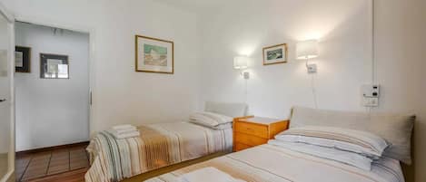 Une chambre d’hôtel avec deux lits, un plancher en bois, une porte et des tableaux encadrés aux murs.