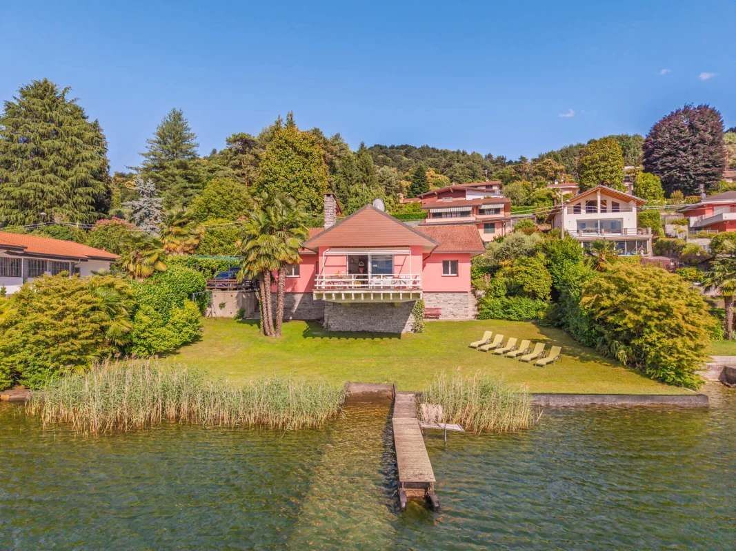 Una casa de techo rojo, rodeada de abundante vegetación y un pequeño estanque con un muelle.