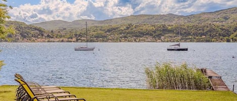A lakeside view with lounge chairs, a dock, and sailboats.