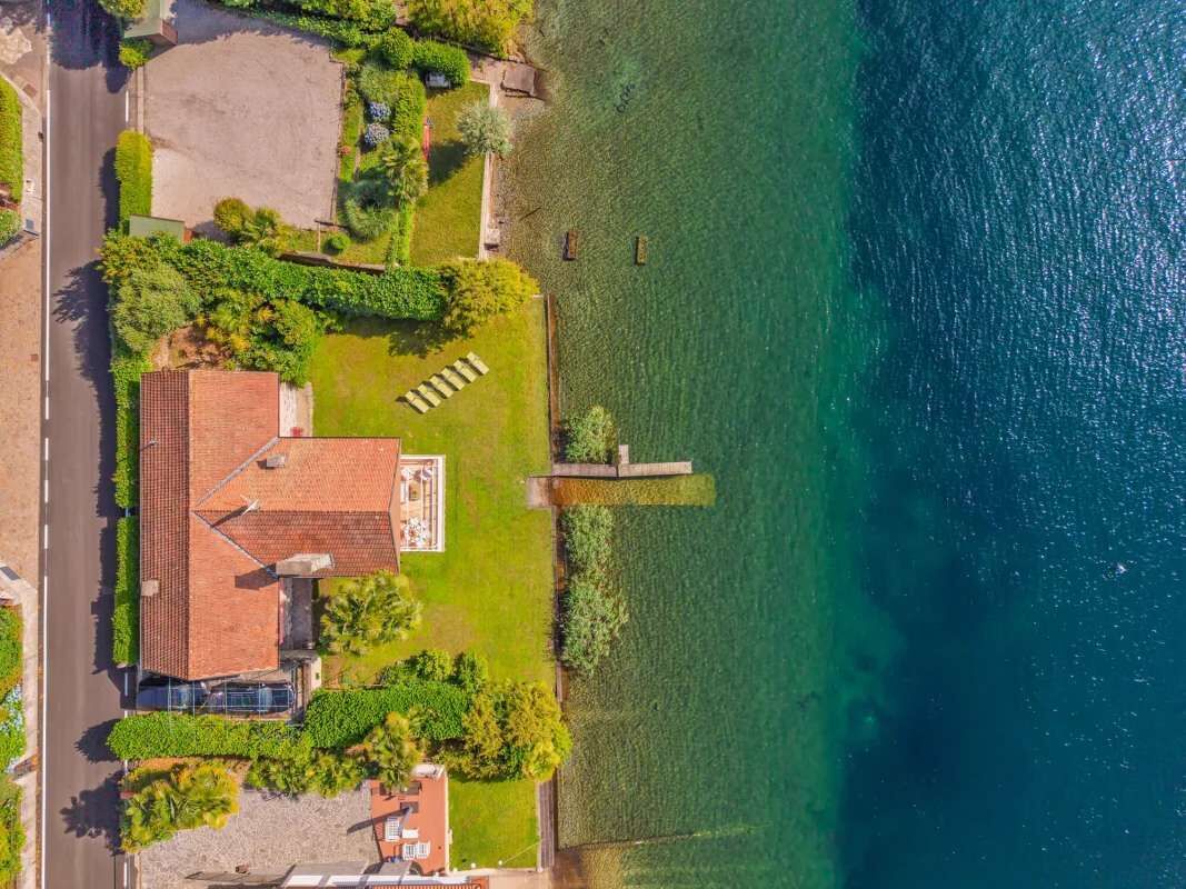 Ett flygbildsfoto av ett bostadsområde med ett hus, en asfalterad uppfart och en vattenyta.