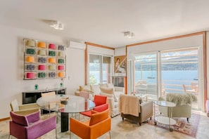 A modern living room with a glass table, colorful chairs, a sofa, and a view of the sea. - Italian Lakes Lakeside Villa With Direct Lake Access (Ranco)