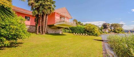 A house with a red exterior, a balcony, and a well-maintained lawn.