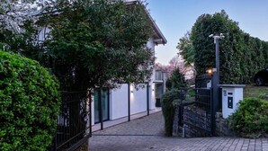 Un chemin pavé mène à une entrée fermée par un portail, avec un petit bâtiment et une caméra de surveillance.