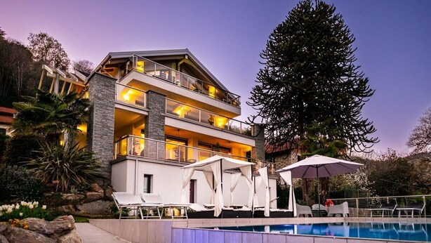 Ein mehrstöckiges Hotel mit Poolbereich, Sitzgelegenheiten im Freien und einem großen Baum.
