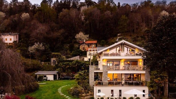 Une maison à plusieurs étages avec une piscine, entourée d’un jardin et d’une colline boisée.