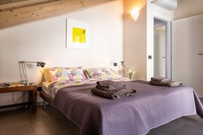 Ein Schlafzimmer mit Bett, Kissen, Nachttisch, Lampe und einer Wandleuchte.