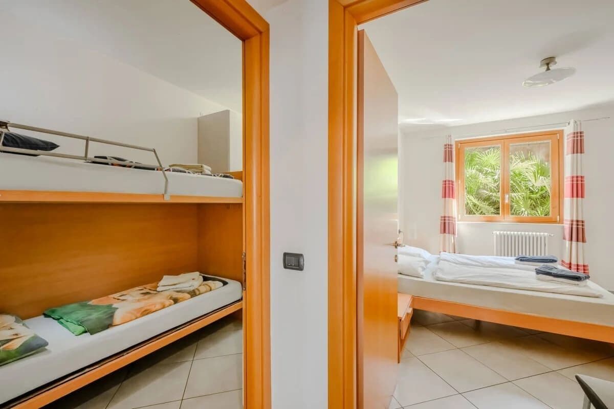 A room with two beds, one on the left and one on the right, a window with curtains, and a radiator.