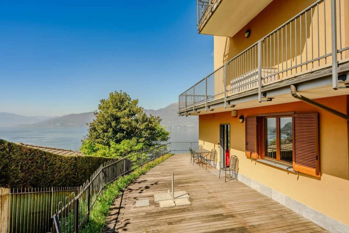 A balcony with a view of the sea, a wooden deck, and a building with a balcony.