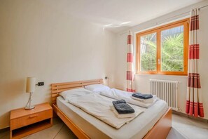 A bedroom with a wooden bed, a bedside table, a lamp, and a window with curtains. - 3 Bedroom Italian Lakes Apartment (Brezzo di Bedero)