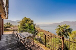 A balcony with a table and chairs, overlooking a lake and mountains. - 3 Bedroom Italian Lakes Apartment (Brezzo di Bedero)