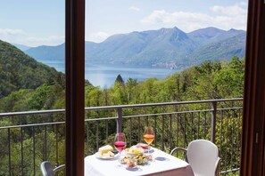 Mesa posta com comida e bebidas numa varanda com vista para uma paisagem montanhosa.