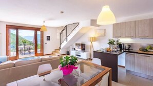 A modern living room with a glass dining table, a sofa, and a staircase leading to an upper floor. - Dumenza Villas (Dumenza)