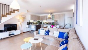 A modern living room with a sofa, coffee table, and TV, connected to a kitchen with a dining area and staircase. - Dumenza Villas (Dumenza)