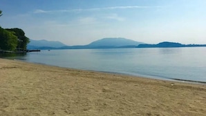 Ein Strand mit blauem Himmel, ruhigem Wasser und Bergen im Hintergrund.