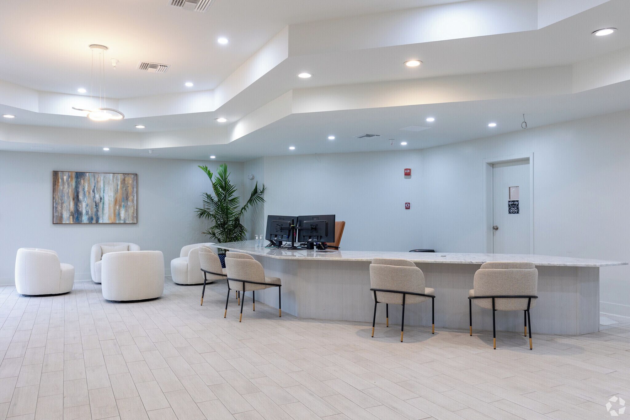 Una moderna area reception con un bancone curvo, diverse poltrone, una pianta grande e un quadro appeso al muro.