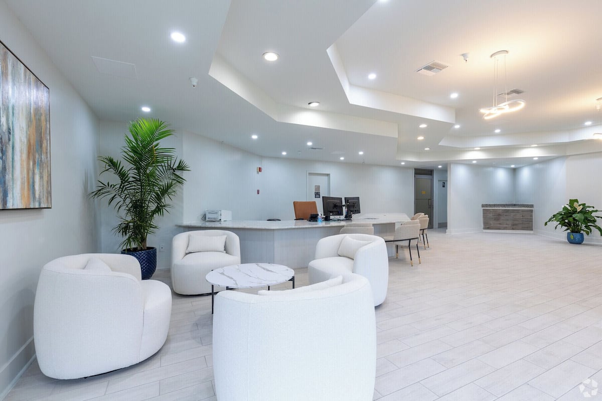 A modern lobby with white furniture, a reception desk, and ceiling lights.