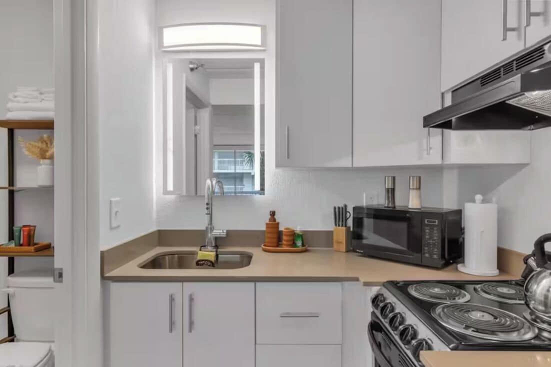 A modern kitchen with white cabinets, a stainless steel sink, a microwave, and a stove.