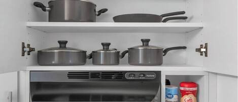 A kitchen with stainless steel pots and pans on shelves, a NuTone appliance, and a coffee maker.