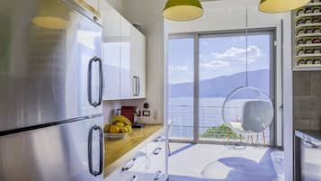 A modern kitchen with stainless steel appliances, a wooden countertop, and a view of the sea through a large sliding glass door.