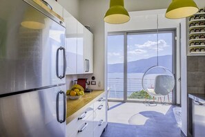 A modern kitchen with stainless steel appliances, a wooden countertop, and a view of the sea through a large sliding glass door. - Pallanza Villas (Verbania)