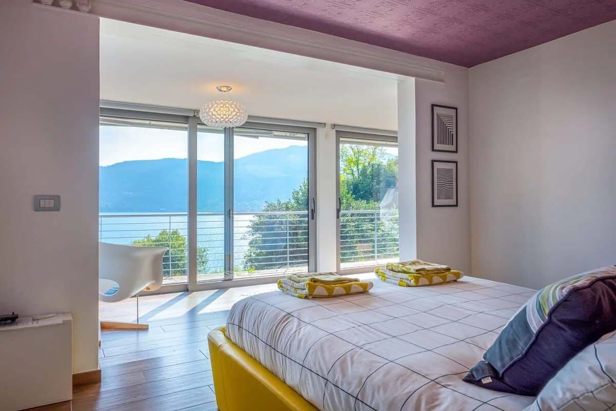 A bedroom with a large bed, a view of the sea, and a balcony with a chair.