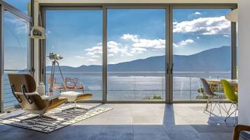 A modern room with a large sliding glass door leading to a balcony with a view of the sea and mountains.