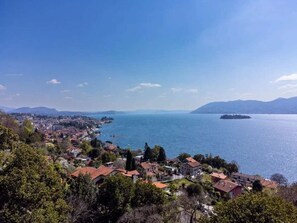 A coastal town with buildings along the shoreline, a clear sky, and a large body of water. - Pallanza Villas (Verbania)