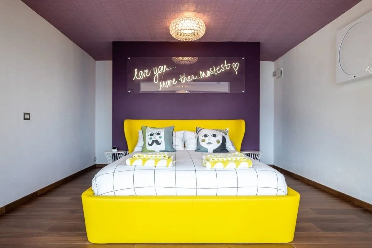 A bedroom with a bed, a neon sign, and a chandelier.