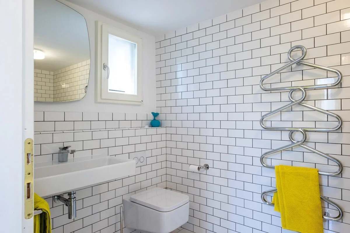 Ein Badezimmer mit weißen Fliesen, einem weißen Waschbecken, einer Toilette und einem Spiegel.