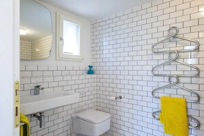 A bathroom with white tiled walls, a white sink, a toilet, and a mirror. - Pallanza Villas (Verbania)