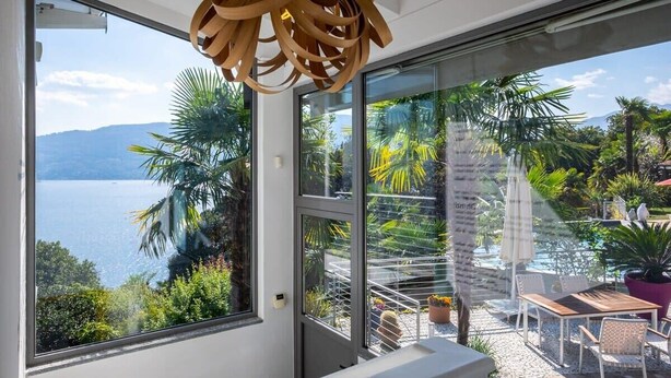 A balcony with a view of a lake and mountains, a wooden ceiling light, and outdoor furniture. - Pallanza Villas (Verbania)