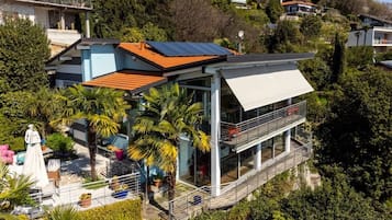 A modern house with a balcony, surrounded by lush greenery and other residential buildings.