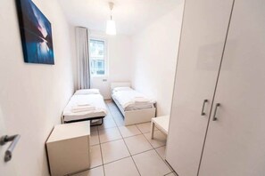 Una habitación de hotel con dos camas individuales, un armario, una mesita de noche y una ventana con cortinas.