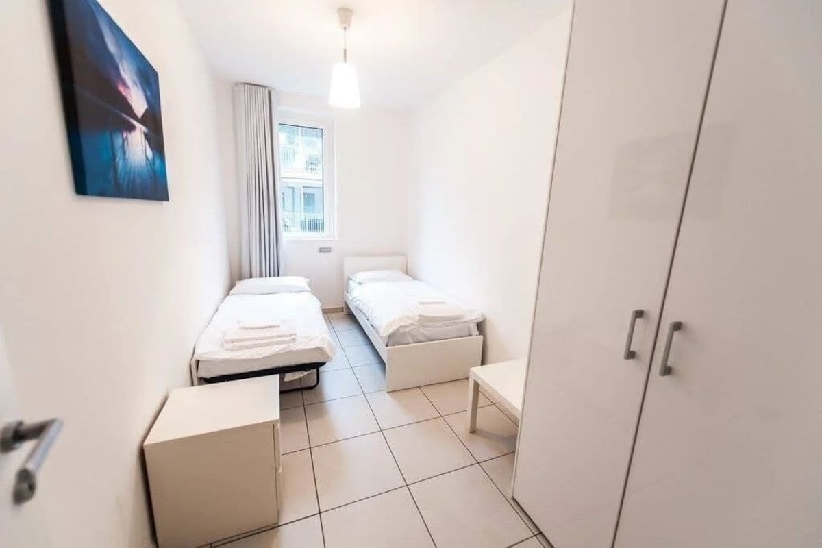 A small, clean room with two beds, a wardrobe, and a window.